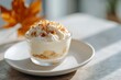 © World of AI - Serving of banana pudding in a clear glass bowl, topped with whipped cream and crushed nuts, beautifully presented on a white plate with a warm autumn ambiance
