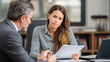 © valeo5 - A tense, focused portrait of a young businesswoman sitting across from a male colleague or advisor, holding a document with a serious, scrutinizing, or skeptical expression.