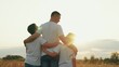 © Victoriia - Children sons hug father outdoors. Young boys hug dad in sunny field. Father loves sons, happy dad hugs. Family walk outdoors. Family, dad, teenage kids walk together in sunny park. Parent of boy