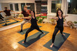 © phoenix021 - Group of three people, two women and young man practicing yoga indoors, doing warrior yoga pose