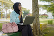 © Fajar - Young Muslim woman wearing a hijab diligently studying outdoors on a park bench with her laptop and books, embracing a modern lifestyle of remote learning and higher education