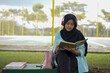 © Fajar - Serene young woman in a hijab and red headphones, deeply engrossed in reading a book while studying outdoors on a tranquil park bench, fostering knowledge and personal growth