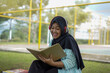 © Fajar - Serene young woman in a hijab and red headphones, deeply engrossed in reading a book while studying outdoors on a tranquil park bench, fostering knowledge and personal growth