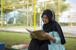 © Fajar - Serene young woman in a hijab and red headphones, deeply engrossed in reading a book while studying outdoors on a tranquil park bench, fostering knowledge and personal growth