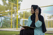 © Fajar - Serene young woman in a hijab and red headphones, deeply engrossed in reading a book while studying outdoors on a tranquil park bench, fostering knowledge and personal growth