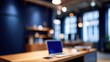 © kokocur - Blurry view of a modern office space.  Wooden desk with laptop,  blue walls,  warm lighting,  shelving,  and windows