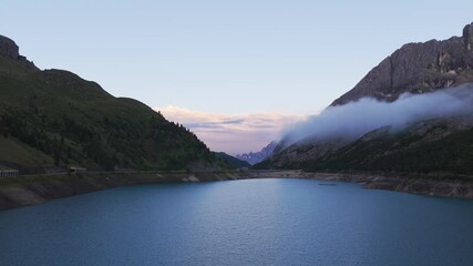 Wall Mural - Fedaia Lake at dusk, Marmolada mountain, and misty clouds in Dolomites, Italy. Aerial drone, copy space