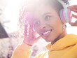 © halayalex - Beautiful woman with afro curls hairstyle.Smiling model in yellow hoodie.Sexy carefree female enjoying listening music in wireless headphones.Posing on street background at sunset