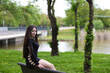 © @skuder_photographer - Latin woman, young and beautiful brunette dressed in black sitting on the back of a park bench looks mysteriously and sensually backwards. In the background a lake on a gray day.