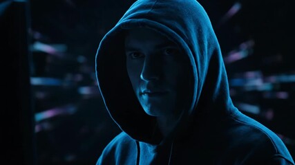 Wall Mural - Hooded man hacking computer with focused expression in dark, futuristic digital environment, technology security concept footage.