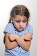 © Niko_Dali - A young girl with a sad expression, arms crossed, looking down.