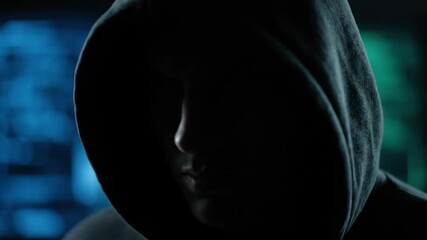 A man in a dark hoodie looking down with focus as a hacker, showcasing cybersecurity and technology, footage