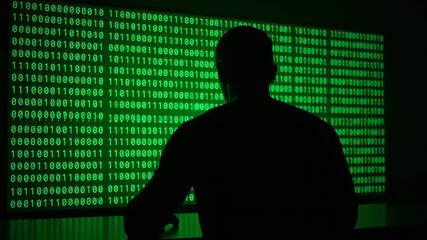 Wall Mural - Man hacker in silhouette works with green binary code on big screen, a conceptual technology and cybersecurity video footage.