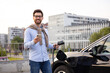 © sofiko14 - A man smiles while holding his phone and an EV charging cable next to his electric car.