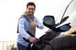© sofiko14 - A man smiles and gives a thumbs up while charging his electric vehicle, promoting sustainable transportation.
