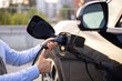 © sofiko14 - A person plugs an electric vehicle into a charger, giving a thumbs up, symbolizing approval and satisfaction with the charging process.
