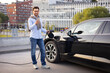 © sofiko14 - A man smiles while charging his electric vehicle at a charging station in an urban setting.