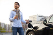 © sofiko14 - A man smiles while holding his phone and charging his electric vehicle at a charging station.