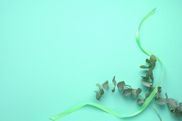 Wall Mural - Beautiful light green ribbon and eucalyptus branches on turquoise background, flat lay. Space for text
