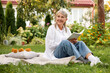 © New Africa - Senior woman reading book on blanket in garden, space for text