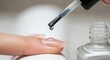 © logonv - Clear top coat nail polish drop on woman finger during manicure procedure. Professional beauty treatment at nail salon concept.