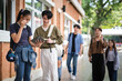 © wattana - Two university students discussing notes and studying together outside a campus building.