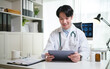 © wattana - Confident doctor analyzing medical information on tablet while sitting at desk in bright clinical workspace.