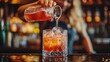 © medalinebow - Bartender skillfully pouring a refreshing cocktail into a glass filled with ice at a lively bar setting