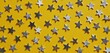 © Yusuf - Overhead shot of numerous silver stars scattered across a bright yellow background. The texture is smooth