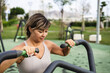 © ADDICTIVE STOCK - Woman exercising outdoors on urban fitness machine