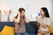 © Thitiporn - Angry woman shouting into a megaphone at her friend covering ears in pain. Concept of noise pollution, argument, stress, communication problems in relationships. Dramatic emotional reaction at home.