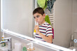 © C&A - Young boy brushing his teeth with electric toothbrush in home bathroom mirror