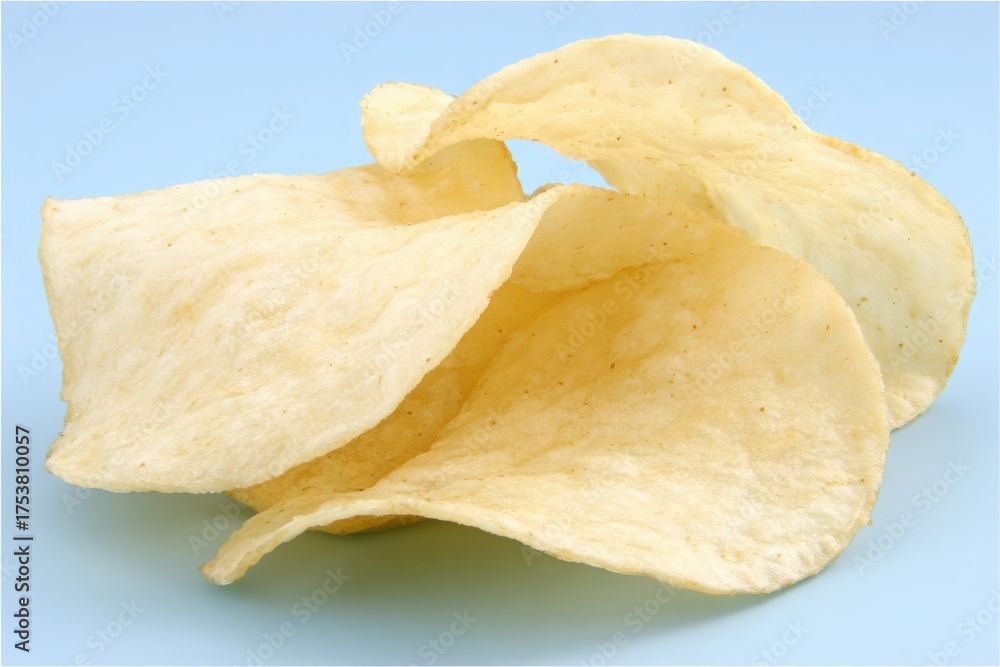 Perfectly shaped potato chips lay piled together against a soft blue backdrop. Their light golden color and crisp texture make them an appealing snack choice for any occasion.