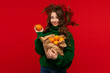 © Vagengeim - Young girl in a green sweater holding oranges in a paper bag, lifting one fruit, wearing a berry wreath