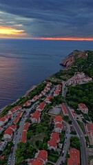 Wall Mural - An aerial portrait of Dubrovnik’s coastline captured during a golden Mediterranean sunset — steep cliffs, deep green pines, and the calm shimmer of the Adriatic stretching endlessly into the horizon.