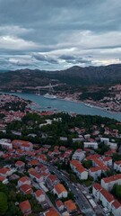 Wall Mural - Aerial drone pans right over Dubrovnik cruise port, capturing trees, houses, and surrounding mountains glowing warmly in golden light during a calm autumn sunset along the scenic Adriatic coastline.