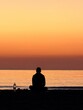 © Aliona Ryne - Person meditating on beach at sunset in peaceful solitude by the sea horizon.