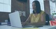 © vectorfusionart - Typing mature Asian woman using silver laptop at modern open-plan office desk, with coffee cup