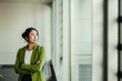 © Westend61 - Businesswoman in green jacket looking out window in modern office