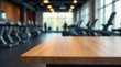 © Kukar Studio - Warm wooden surface in the foreground presents a calm visual, contrasting the blurred interior of a modern fitness facility, showcasing exercise equipment and active individuals.