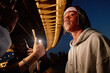 © Seventyfour - Portrait of young Black man standing under bridge at night, looking away from camera while being photographed with smartphone by another, urban evening setting visible