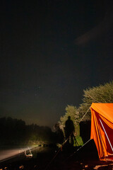 Wall Mural - A person is standing in front of an orange tent. The tent is set up in a forest