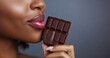 © TENphoto - Woman enjoying a piece of dark chocolate with a sensual expression
