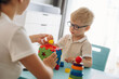 © standret - Composes logic puzzles. Speech therapist is with young boy indoors
