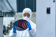 © metamorworks - A female worker in protective clothing inspects silicon wafers at a semiconductor factory