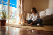 © Taras Grebinets - Woman Writing in a Cozy Home Living Room With Natural Light and Plant on Floor