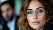 © Yuliia - Young woman with blue eyes wearing stylish round glasses frames, natural makeup, and wavy brown hair looking confidently at camera against blurred background.