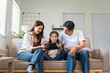 © amnaj - Happy Asian family spending bonding time. Parents and daughter sitting on couch, watching and learning on digital tablet