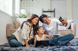 © amnaj - Asian family sitting on floor, happy parents and child smiling and bonding while taking a selfie with a mobile phone