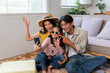 © amnaj - Asian family sitting on floor, preparing for travel, making video call on smartphone, feeling excited for holiday